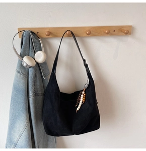Detail of black suede hobo bag hanging with stylish bead charm and lifestyle props