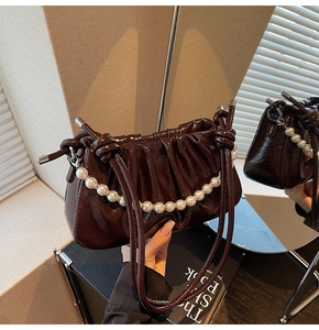 Detail of coffee brown patent leather pleated bag with decorative pearl chain strap