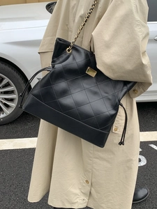 Chic black quilted leather tote bag with gold chain strap shown on person in street style