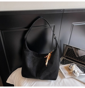 Close-up of black suede hobo bag with colorful wooden bead charm in an office setting