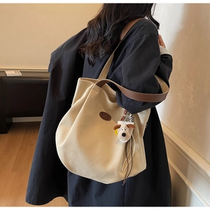 Close-up of cream canvas tote bag with brown leather handles and a plush puppy charm