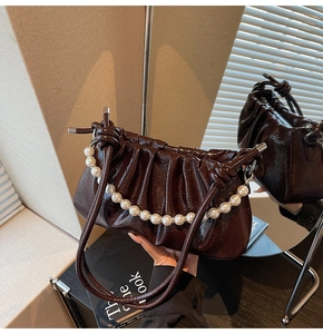 Detail of dark brown pleated cloud bag with pearl chain and glossy leather texture