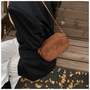 Close-up of brown suede crossbody bag with vintage gold zippers on an autumn background