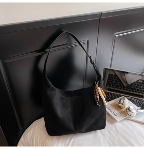 Detail of black suede hobo bag with wooden bead charm and minimalist aesthetic style