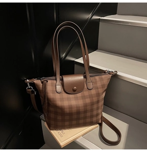 Detailed view of brown plaid tote bag with leather handles on artistic book props