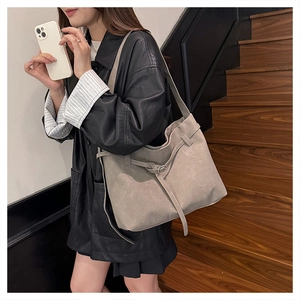 Detailed view of grey matte leather tote bag worn by a model in black leather jacket