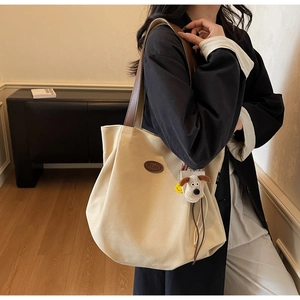 Detail of beige canvas tote with brown leather straps and cute puppy plush pendant