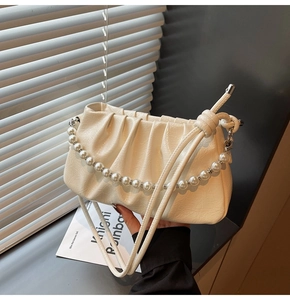 Detail of cream pleated cloud bag featuring decorative pearl chain and thin leather strap