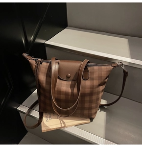 Detail of brown checkered tote bag with leather flap, zip closure, and adjustable strap