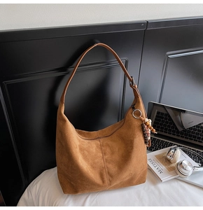 Close-up of brown suede hobo bag with wooden bead charm on a minimalist white bed
