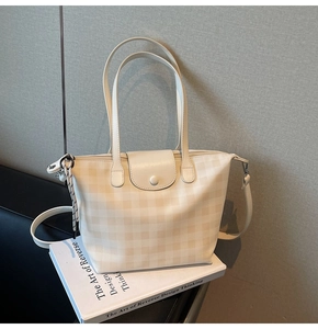 Close-up of checkered pattern tote bag with metal charm and adjustable shoulder strap
