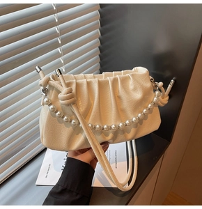 Detail of off-white pleated cloud bag with pearl chain and knotted strap on windowsill