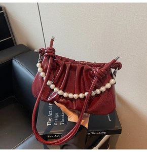 Detail of burgundy ruched shoulder bag with pearl chain and glossy leather texture