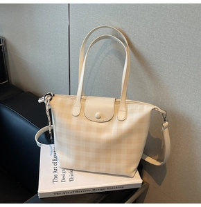 Detail of checkered tote bag with leather handles and flap on a decorative prop book