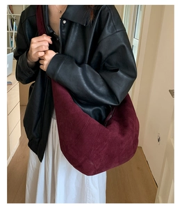 Detail view of large burgundy suede croissant bag worn by a model in casual style