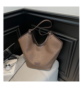 Detail showing the intricate woven texture and leather logo of the brown tote bag