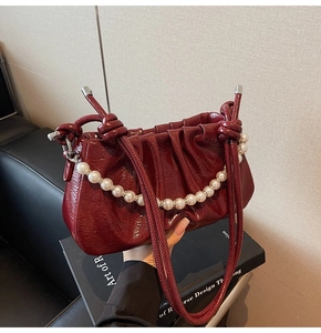 Close-up of wine red pleated patent leather bag with luxury pearl chain and knot handle