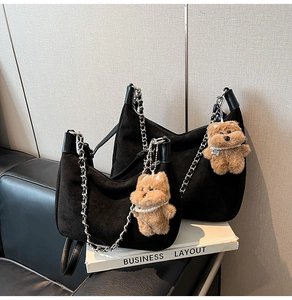 Detail of black suede hobo bag with silver chain strap and plush bear charm accessory