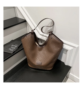 Detailed view of brown woven leather texture and logo plaque on a stylish tote bag