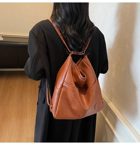 Close-up of a brown leather backpack with embossed logo and side pocket on a model