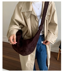 Detail of a large dark brown suede hobo bag styled with a trench coat and casual jeans