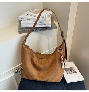 Detail view of brown suede hobo bag with a beaded tassel charm on textured fabric