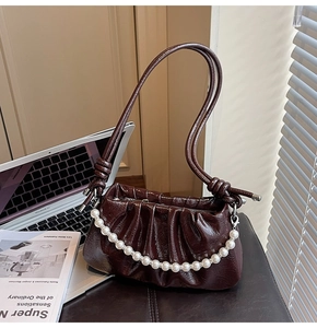 Detail of dark brown patent leather shoulder bag featuring a white pearl decorative chain