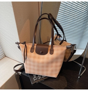 Close-up of a checkered tote bag with brown leather handles and a snap closure lid