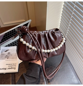 Detail view of dark brown ruched cloud bag featuring pearl chain and glossy leather texture