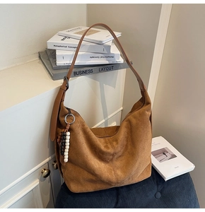 Macro detail of brown suede hobo bag with adjustable leather strap and beaded charm