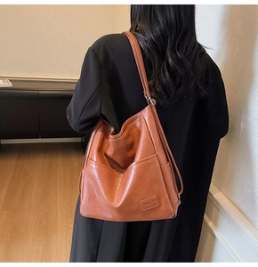 Detail view of the brown leather tote bag showing a fashion patch and side pocket stitching
