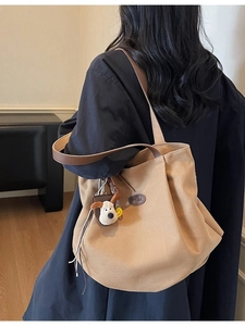 Large khaki canvas tote bag with brown leather handles and plush puppy keychain detail