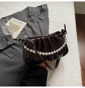 Detail of dark brown patent leather pleated cloud bag with elegant pearl chain accessory