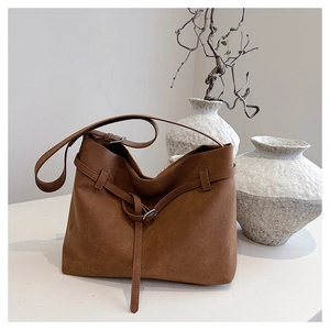 Detail of brown suede tote bag with decorative metal buckle belt and slim shoulder strap