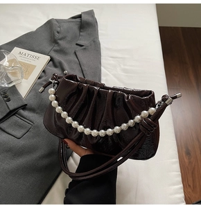Detail of dark brown pleated handbag with pearl strap and glossy patent leather finish