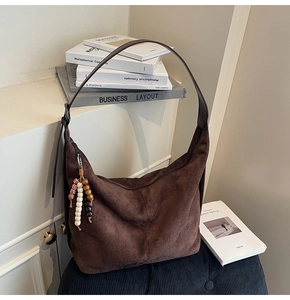 Detail of a dark brown suede hobo bag featuring a wooden bead tassel on a soft cushion