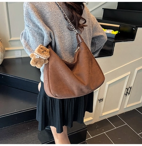 Close-up of brown suede hobo bag with silver chain strap and plush bear pendant detail