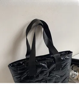 Detail of the black quilted tote bag featuring wide nylon straps and wavy stitching texture