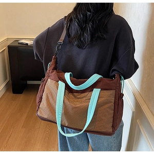 Rear view of a large brown tote bag with plaid pockets and blue straps on a model