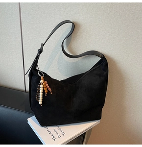 Detail of black faux suede hobo bag with ethnic wooden bead charm on white book