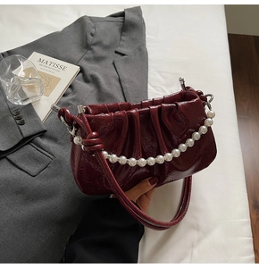 Detail of burgundy ruched hobo bag with glossy finish and elegant pearl handle