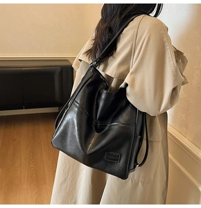 Rear view of model wearing a black vintage leather tote bag with stylish square logo patch