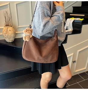 Close-up of brown suede shoulder bag featuring a metal chain strap and cute bear pendant