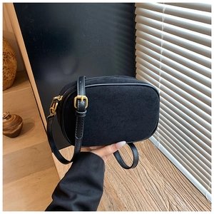 Detail of a vintage black suede crossbody bag with gold buckle and adjustable strap