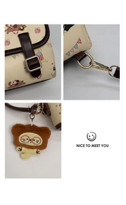 Vue détaillée du sac beige à imprimé dessin animé, ferrures dorées et charm ours en peluche