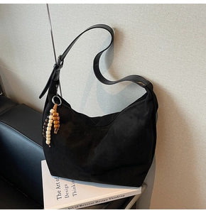 Detail of minimalist black suede hobo bag with unique beaded wooden charms and wide strap