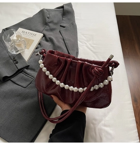 Detail of burgundy ruched leather shoulder bag with elegant large pearl handle decoration