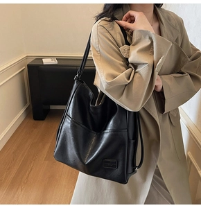 Detail of high-capacity black leather tote bag worn with a khaki coat in a minimalist room