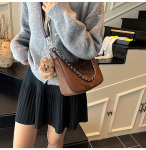 Detail of brown faux suede crescent bag with silver chain and cute teddy bear charm