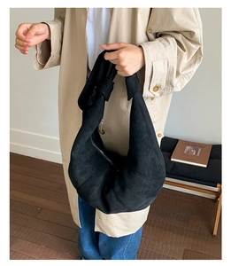 Close-up of black suede hobo bag with wide shoulder strap and knot detail in room